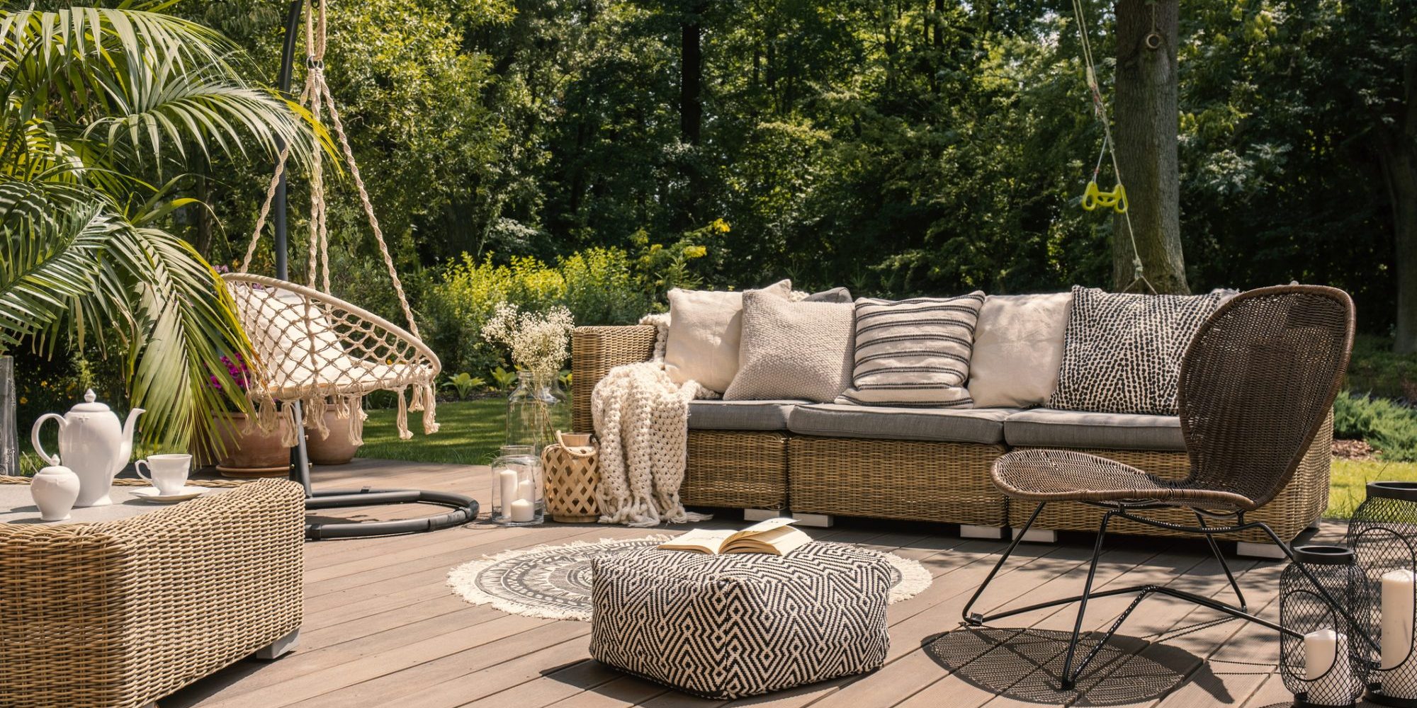 A rattan patio set including a sofa, a table and a chair on a wooden deck in the sunny garden. concept