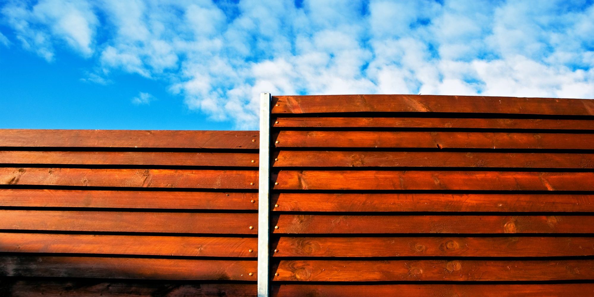 Wooden fence or boarding with cloudy blue sky in background - modern design. Wood construction.